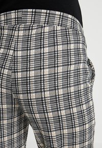 Byxor med ett svart och beige rutmönster. Tillverkade av ett texturerat tyg med en figurnära design och en slät midja.