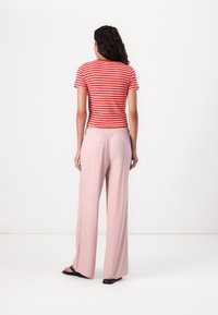 Haut à manches courtes rayé rouge et blanc associé à un pantalon large rose clair, en tissu lisse, avec taille élastique et des sandales noires.
