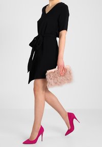 Svart kortärmad klänning med knytbälte, matchad med rosa stilettklackar och en ljusrosa fällväska i konstpäls.