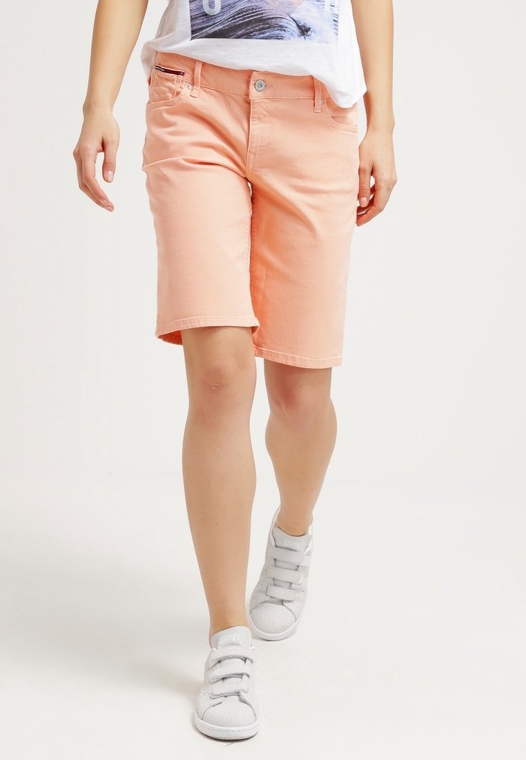 Shorts de mezclilla color durazno, con corte recto, bolsillos frontales y un solo botón. Combinados con zapatillas grises de velcro.