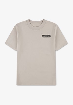 Jasnobeżowa koszulka z krótkim rękawem wykonana z bawełny. Na piersi znajduje się czarny napis: „ABERCROMBIE QUALITY GOODS SINCE 1892.”