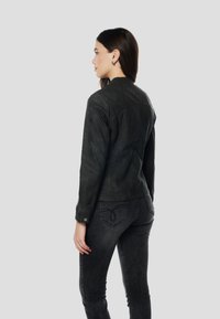 Čierna kožená bunda s priliehavým strihom, zapínaním na patentky a textúrovanými detailmi. Nosí sa s tmavosivými džínsami, pohľad zozadu.