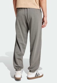Grå bomulds joggingbukser med elastiske manchetter, sidesømme og en afslappet pasform, parret med hvide sneakers med sorte striber og en struktureret sål.