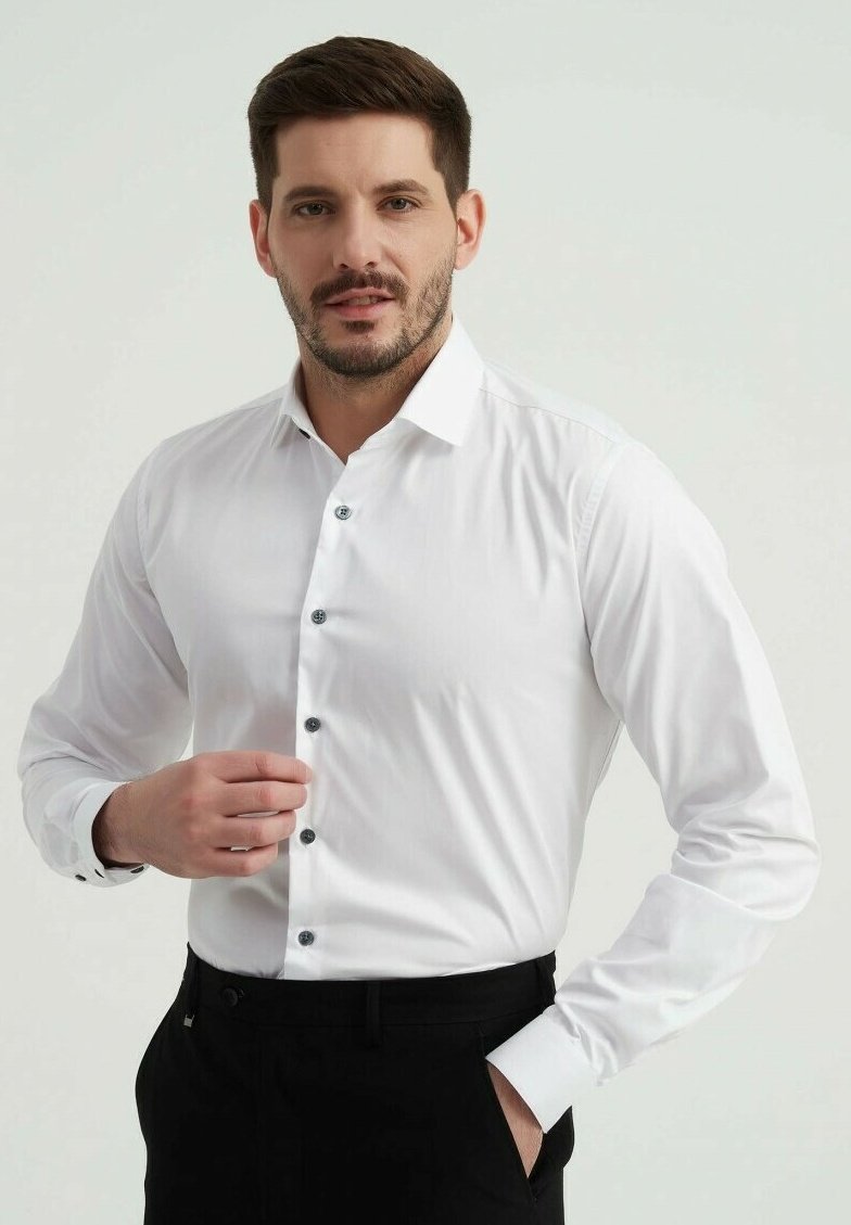 Chemise blanche à manches longues en tissu lisse, avec des boutons foncés et un col classique. Portée avec un pantalon noir.