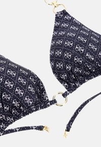 Navy bikini top with white geometric pattern, gold hardware accents, and adjustable ties. Features soft, gathered fabric and ring detailing.