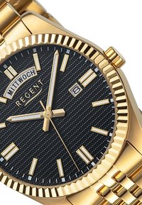 Montre dorée avec un cadran noir texturé, des index lumineux et un affichage de la date. Elle présente un bracelet en métal et un design de lunette cannelée.