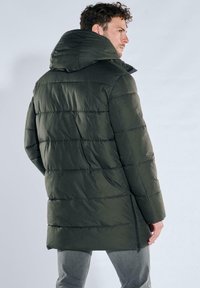 Dark green puffer jacket with a high collar, horizontal stitching, side zipper pockets, and a relaxed fit. Textured fabric with a smooth finish.
