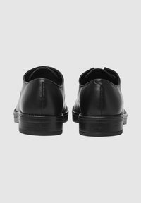 Schwarze Lederschuhe mit glatter Textur, runder Form und niedrigem, gestapeltem Absatz. Sie verfügen über dezente Nähte und eine glänzende Oberfläche.