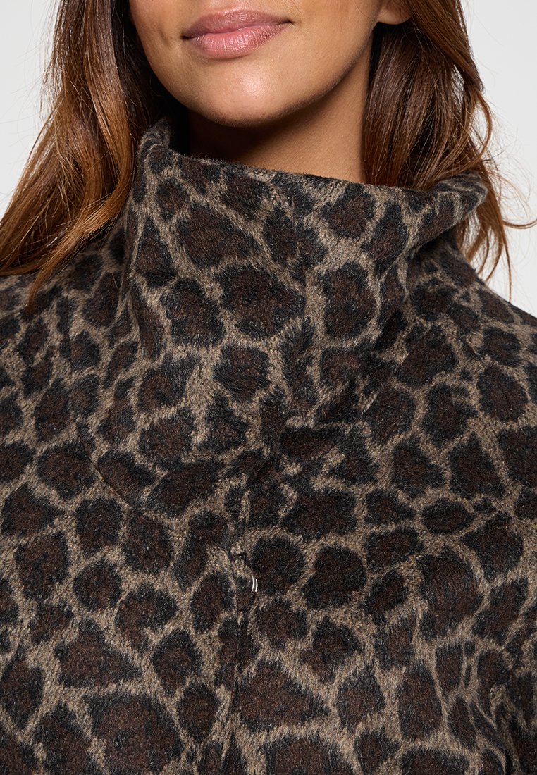 Donna che indossa un maglione leopardato morbido con collo alto, caratterizzato da macchie marroni e nere, mostrando le labbra e parte dei lunghi capelli castani.