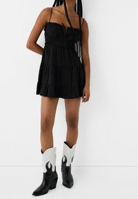 Svart kort klänning med volangkant, tunna band och justerbar knytning. Bärs med svart- och vitrandiga cowboystövlar med flamdekorationer.