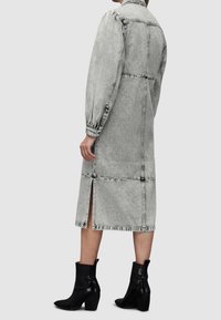 Denim-mekko haalistuneessa harmaassa, jossa on tiukka yläosa, puffatut pitkät hihat ja polvipitkä helma, jossa on sivurei'ät. Yhdistetty mustiin korkokenkiin.