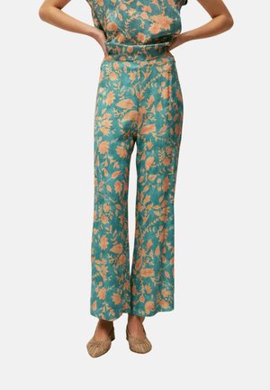 Pantalones teal de pierna ancha con estampado floral en color melocotón, combinados con top sin mangas a juego y zapatos beige tejidos sin cordones.