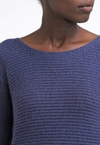 Pull en maille bleu marine avec un large décolleté, présentant un motif côtelé texturé et un tissu doux. Vue en gros plan du matériau et du décolleté.