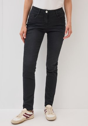 Jeans skinny negros de tiro medio, fabricados con una mezcla de algodón, con bolsillos frontales y cierre de botón metálico. Textura suave y diseño ajustado.
