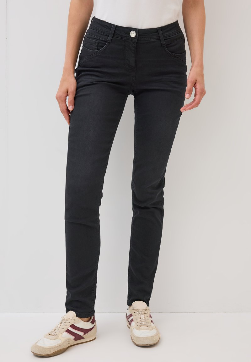 Jeans skinny negros de tiro medio, fabricados con una mezcla de algodón, con bolsillos frontales y cierre de botón metálico. Textura suave y diseño ajustado.