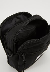 Czarna torba nylonowa z dwoma zamykanymi na zamek komorami, z teksturowanym wykończeniem i czarnymi akcentami. Kompaktowy design odpowiedni do małych przedmiotów.