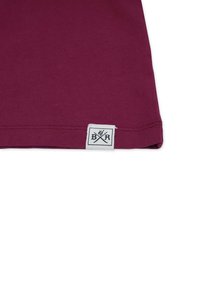 Mørkerød bomulds-t-shirt med en syet kant og et hvidt mærke med et grafisk logo. Glat tekstur og tætsiddende design.