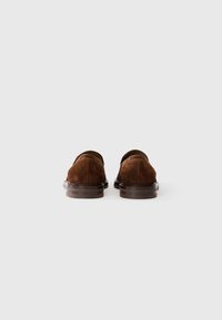 Smeđi zamršeni loafers s glatkom kožnom đonom. Nizak dizajn na stražnjem dijelu, zaobljeni vrh i minimalistički detalji šivanja.