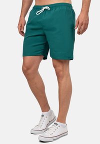 Pantaloni da bagno turchesi con vita elastica, cordoncino regolabile e un logo discreto sul lato. Realizzati in tessuto leggero.