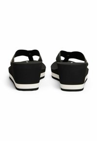 Sandalias de cuña negras con una correa texturizada y una plantilla lisa. La suela de plataforma gruesa tiene una franja blanca de acento para contraste.