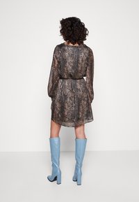 Robe noire et dorée à motif avec une taille cintrée, des manches longues et un ourlet fluide, assortie à des bottes bleu clair jusqu'aux genoux.