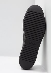 Semelle de chaussure noire avec des lignes de grip texturées et le logo "Clarks". Le matériau semble être du caoutchouc, avec un bout arrondi et un talon légèrement surélevé.