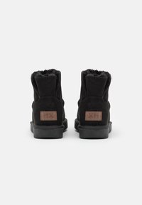 Černé semišové kotníkové boty s kožešinovou podšívkou, texturovanými detaily a hnědým logem na patě. Plná gumová podrážka s mírným vzorkem.