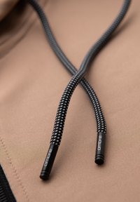 Gros plan sur des cordons de capuche tressés noir et blanc reposant sur un tissu beige avec « OMBRE » imprimé sur les embouts métalliques.