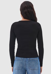 Svart långärmad ribbad topp med en rundad halsringning, visad från baksidan. Matchas med högmidjade blå jeans med bakfickor.