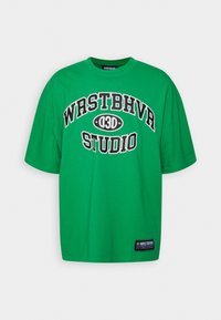 Groene katoenen T-shirt met bold zwarte tekst "WRSTBHVR 030" en "STUDIO" op de voorkant; korte mouwen en een relaxte pasvorm.