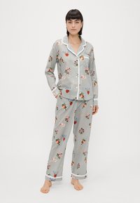 Conjunto de pijama riscado com padrões florais e de frutas. Feito de um tecido suave, inclui uma camisa de botão com colarinho e calças combinando.