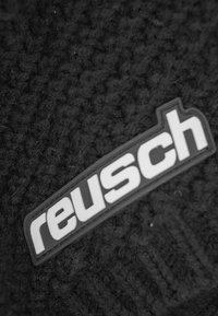 Black fabric with a textured surface featuring a white rubberized logo patch that reads "reusch." The design is simple and minimal.