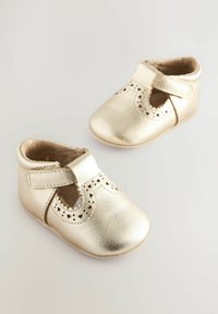 Auksiniai odiniai kūdikių bateliai su perforuotomis detalėmis, apvaliais pirštais ir Velcro dirželiu, leidžiančiu lengvai užsegti, su minkšta smėlio spalvos pamušalu.