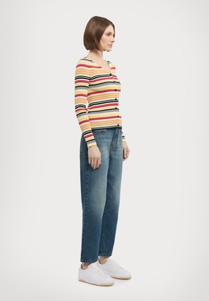 Striped long-sleeve cardigan in yellow, red, and black; paired with loose blue denim jeans and white sneakers with gum soles.