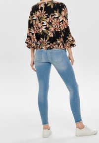 Jeans skinny blu chiaro con effetto sbiadito, orlo finito, abbinati a una blusa nera floreale con maniche arricciate e scollatura a chiave.