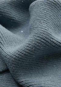 Textureret stof i en dæmpet blå farve, prydet med ribbede mønstre og spredte små perler, hvilket skaber visuel interesse og dybde.