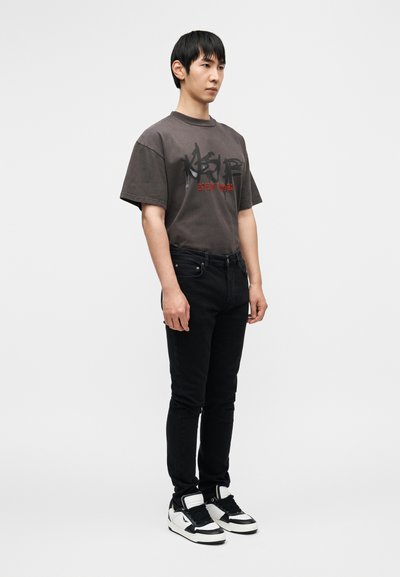 Hall hallipikk T-särk musta ja punase graafilise tekstiga, kombineeritud mustade kitsaste teksapükste ja must-valgete tennistega. Tavaline taust.