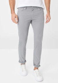 Hellgraue Hosen mit schlankem Schnitt, die eine glatte Textur und hochgekrempelte Säume aufweisen, kombiniert mit weißen Turnschuhen. Klassisches Design mit Fronttaschen.