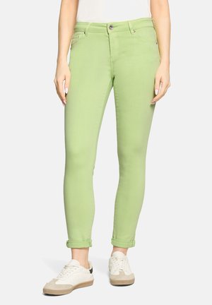 Wąskie, jasnozielone spodnie z podwiniętymi mankietami, noszone z białymi trampkami i białą bluzką, widoczne od talii do stóp.