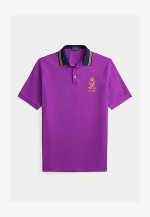 Tricou polo violet cu guler bleumarin, cu dungi galbene, logo brodat auriu cu o coroană și "EST. 1967" pe piept.