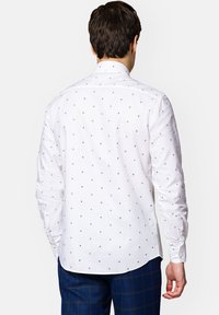 Biała koszula z długim rękawem, z małymi, granatowymi wzorami w kształcie kwiatków, klasyczny kołnierzyk i mankiety na guziki; gładka tekstura materiału.