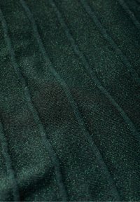 Tessuto verde scuro con una superficie fine e texture che presenta righe verticali. Il materiale ha un leggero luccichio, creando profondità visiva.