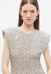 Vestido dourado metálico com corte ajustado, apresentando mangas curtas estruturadas e uma textura integral de lantejoulas que refletem a luz.