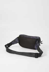 Sac banane noir et camouflage bleu marine avec une texture en maille, une sangle réglable, une fermeture éclair et un détail de cordon sur le côté. Design compact.