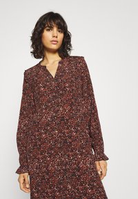 Robe à manches longues avec un imprimé multicolore rouge, noir et blanc, décolletée en V, fermeture à boutons et manches à volants.