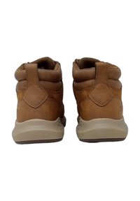 Botas de cuero marrón hasta el tobillo con cuello acolchado, suela de color marrón claro y acentos texturizados. Presentan una forma redondeada y una pestaña de agarre en la parte posterior.