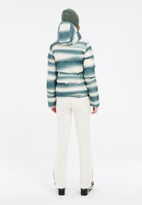 Gepolsterte, gefütterte Jacke mit horizontalen blau-weißen Streifen, kombiniert mit weißen Hosen und schwarzen Skischuhen, die einen sportlichen Winterlook präsentieren.
