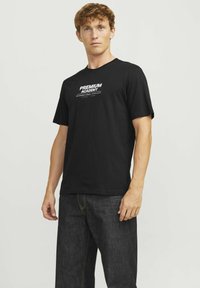 Črna bombažna majica s kratkimi rokavi z belim napisom "PREMIUM ACADEMY" in "INTERNATIONAL CONCEPT" natisnjenim spredaj. Prijeten kroj.