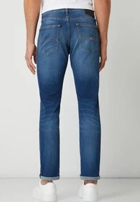 Slim-fit blå denimjeans med medeltvätt, som har två bakfickor och uppvikta fållar, tillsammans med vita sneakers.