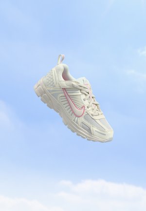 Baskets blanches et rose clair avec semelle texturée et détails en mesh flottant sur fond de ciel bleu clair.